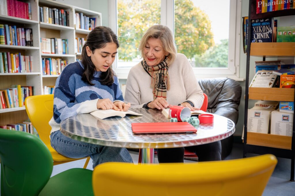 Ein Mädchen und eine Frau an einem Tisch, sie schauen gemeinsam in ein Buch
